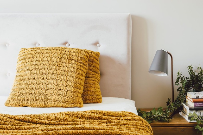 White tufted upholstered headboard with yellow knitted pillows and blankets