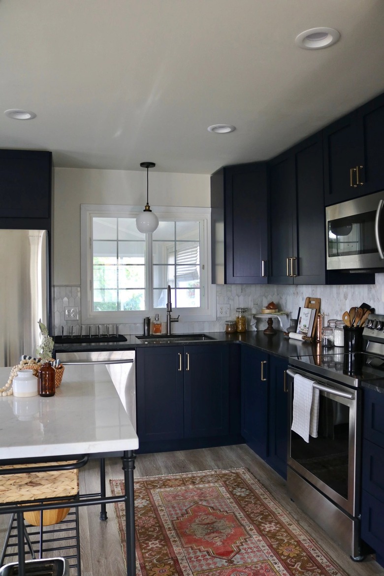 dark navy kitchen cabinets with vintage rug and marble backsplash