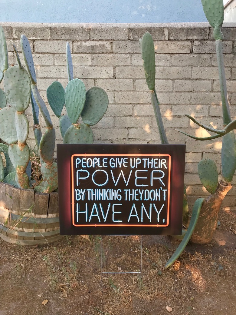 Lawn sign next to cactuses against brick wall.