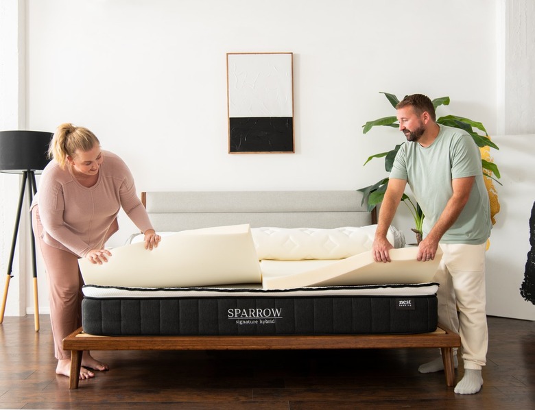 Two people removing the foam padding in the Nest Bedding Sparrow mattress on a dark wood bed frame.