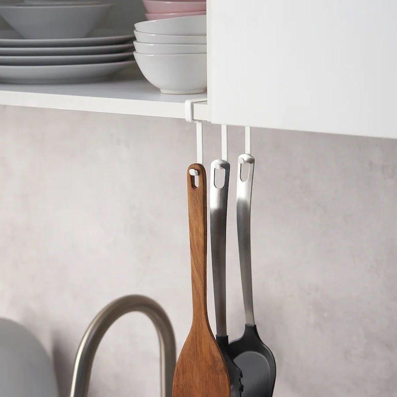 A white hook rack holding spatulas underneath a white upper kitchen cabinet.