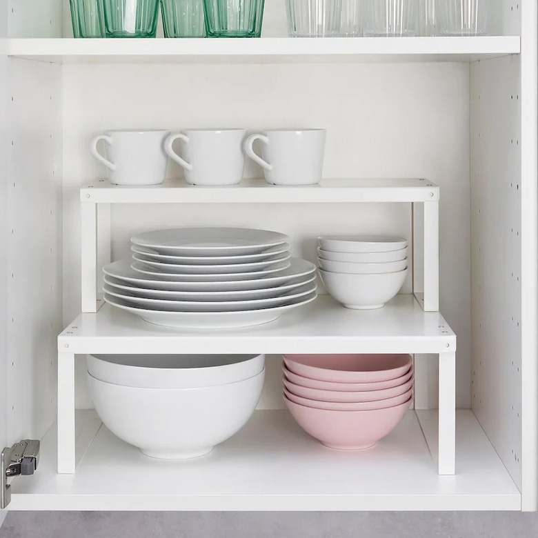 Two white shelf inserts stacked on top of each other in a kitchen cabinet