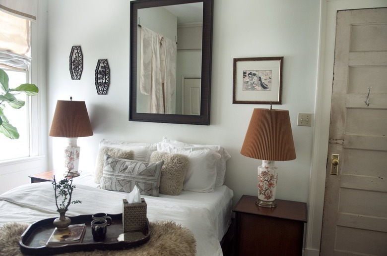 bedroom with two brown lamps and a white bed with pillows and a black framed mirror above