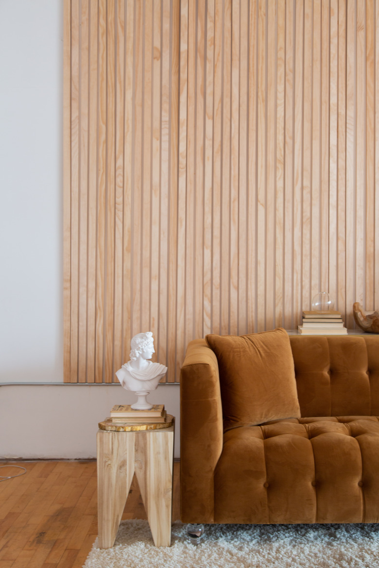 mustard velvet couch with wood side table and bust nearby