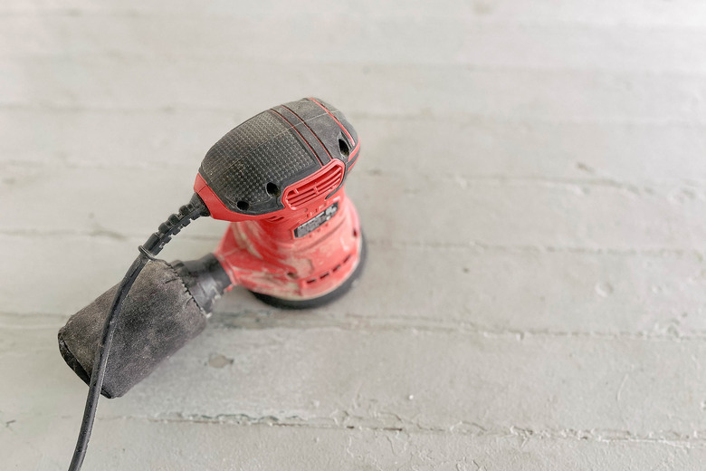 Orbital sander sanding painted wood floor