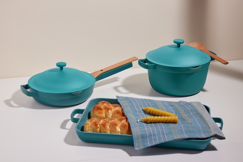 Our Place Shabbat Set on a white table including two loaves of challah in a teal pan covered by a cloth with candlesticks