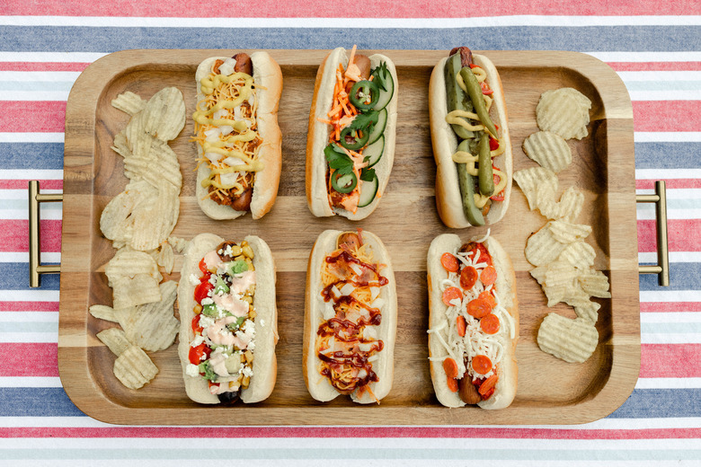 Six gourmet hot dogs plated on wooden serving tray with potato chips