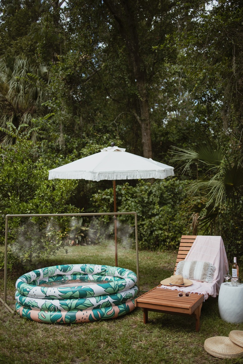 Green PVC pipe water mister over an inflatable pool next to lounge chair and fringe patio umbrella