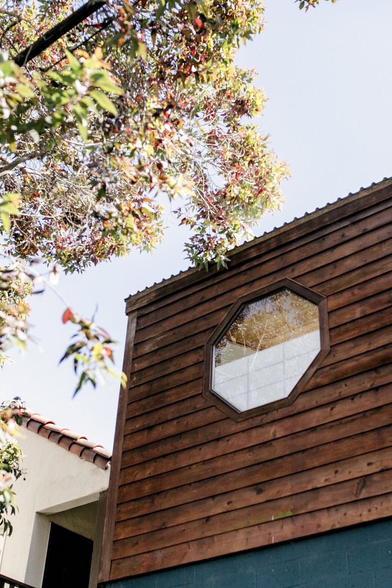 Wood exterior of a house with an octagonal window, by a tree.