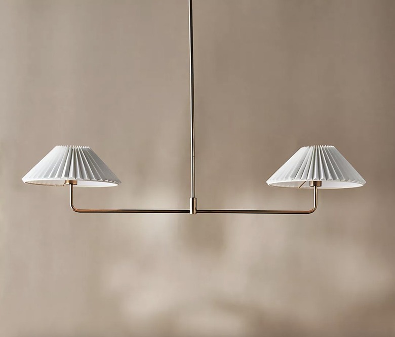 gold two-light chandelier with white shades against a tan wall.