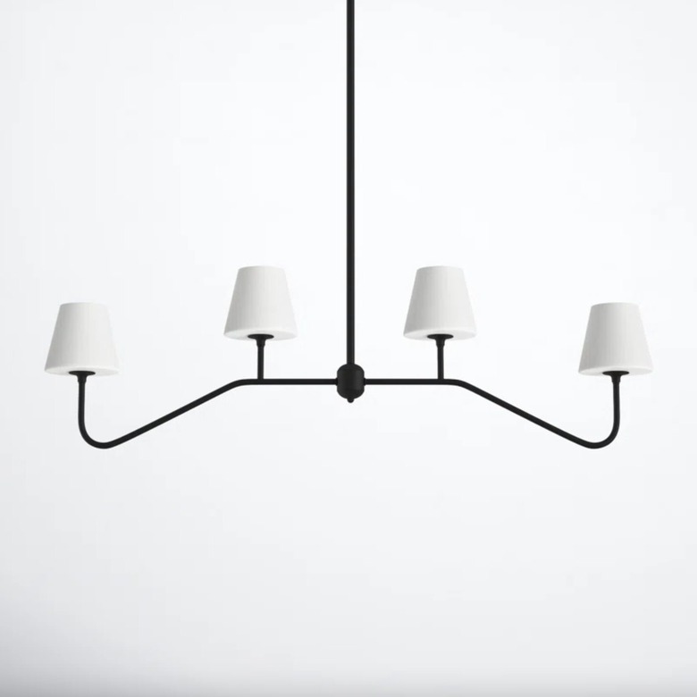 4-light black linear chandelier with white glass shades against a white back wall.
