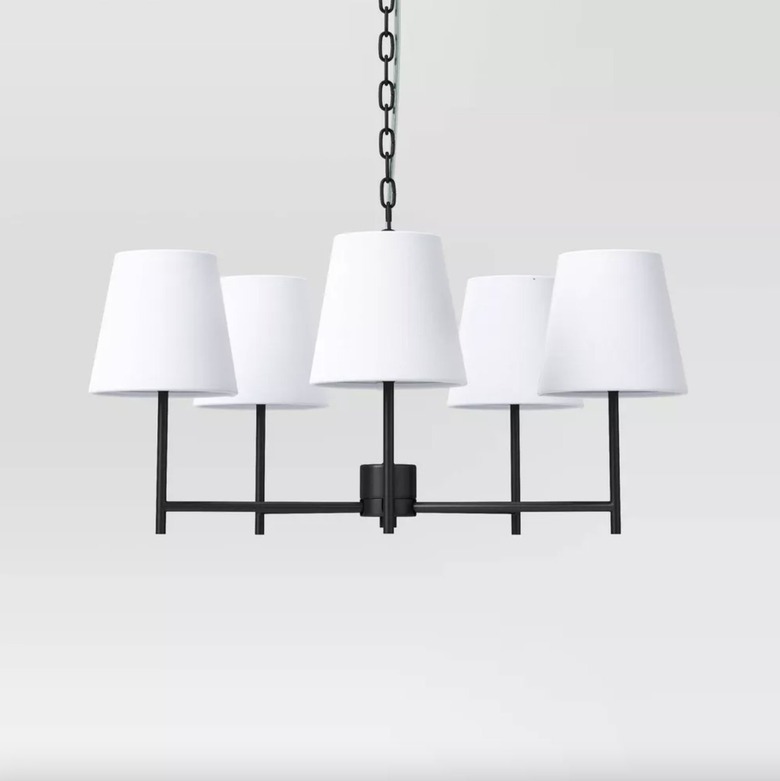5-light black chandelier with white shades against a an off-white backdrop