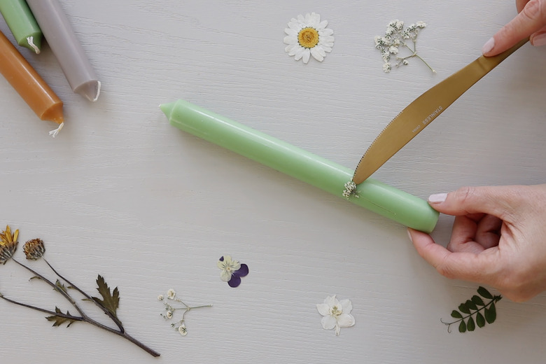 Running hot knife around edges of pressed flower on taper candle