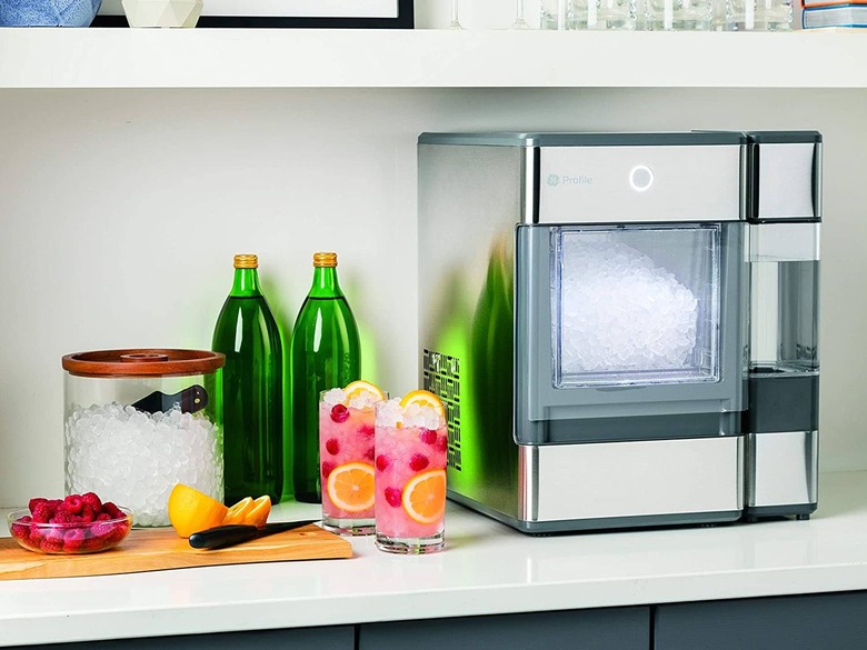 A freestanding nugget ice maker on a countertop next to sparkling water and two cocktails in tumblers