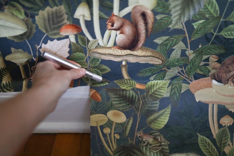 Cutting off excess wallpaper along bottom of wall with a utility knife