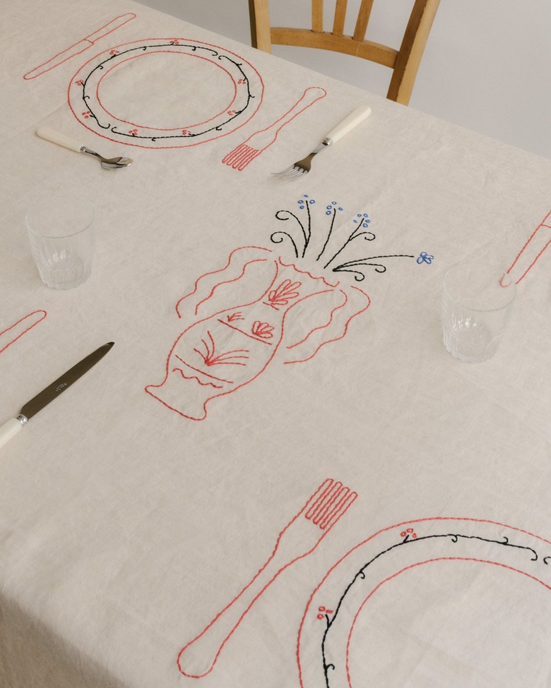 A white tablecloth embroidered with a pink vase of blue flowers