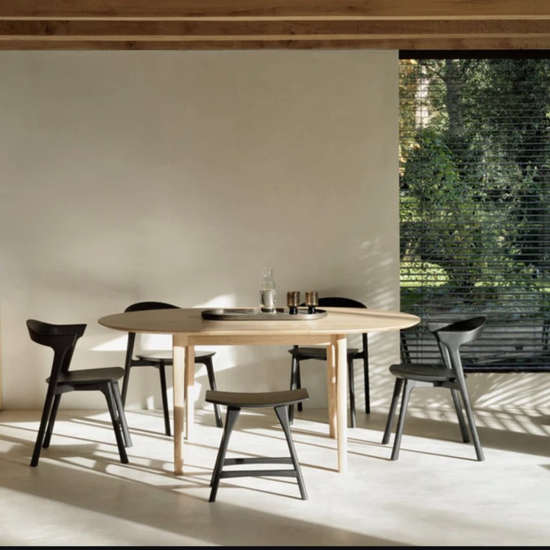 Image of a light-wood oval table surrounded by black chairs and a stool