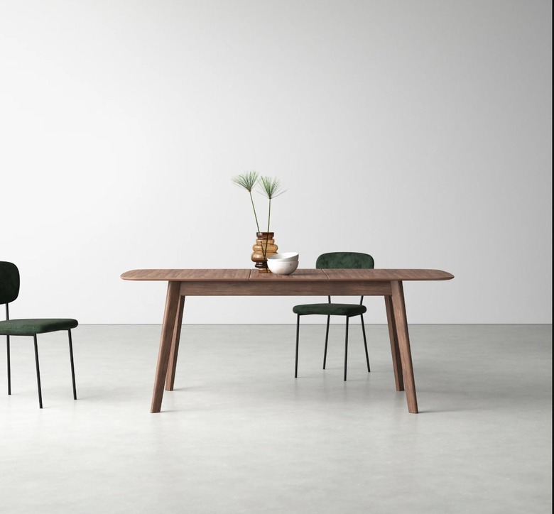Image of Scandinavian extendable dining table with two green chairs. A vase with greenery and two stacked white bowls sit on the table.