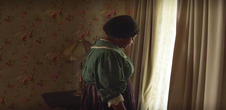 figure standing near curtains with floral wallpaper in the background