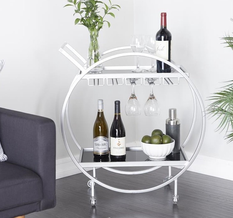 Brushed steel circular shaped bar cart with glassware and bottles.
