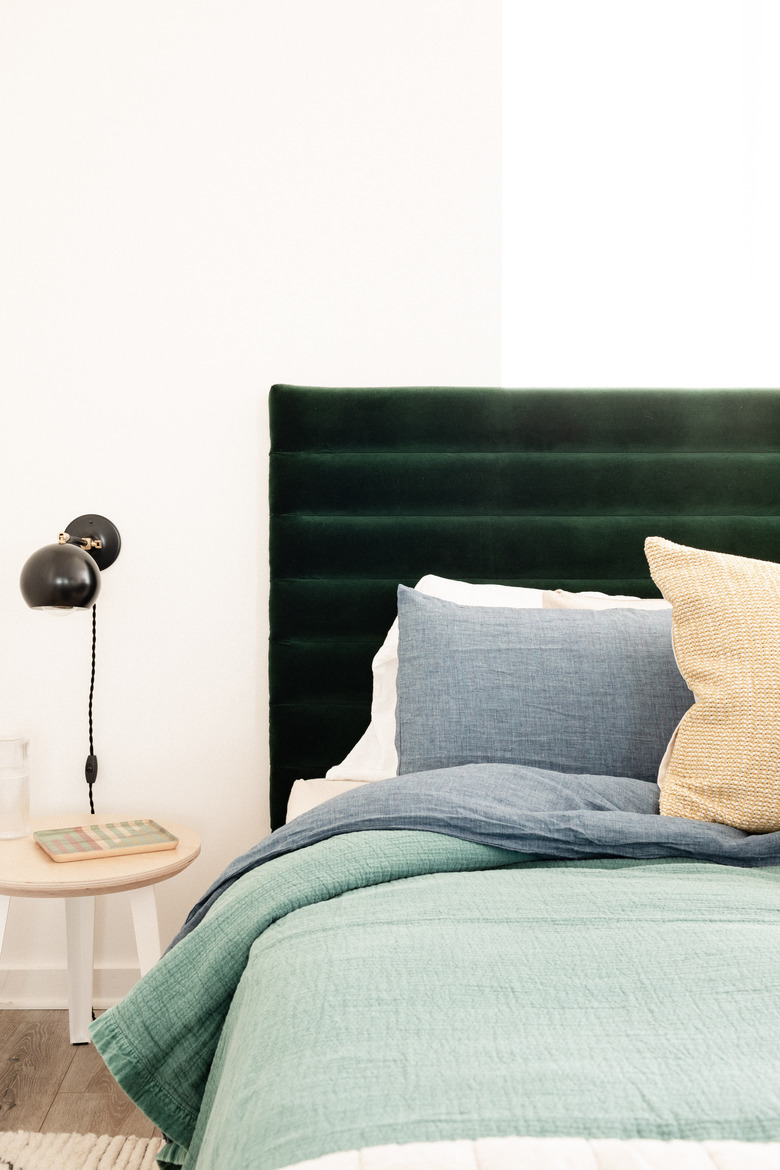 channel tufted headboard in bedroom with black wallsconces and side table