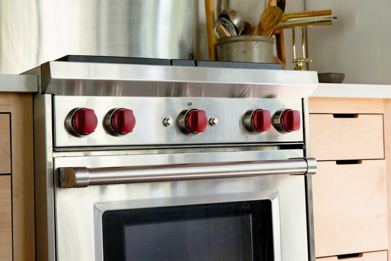 An oven with red knobs. Light wood cabinets