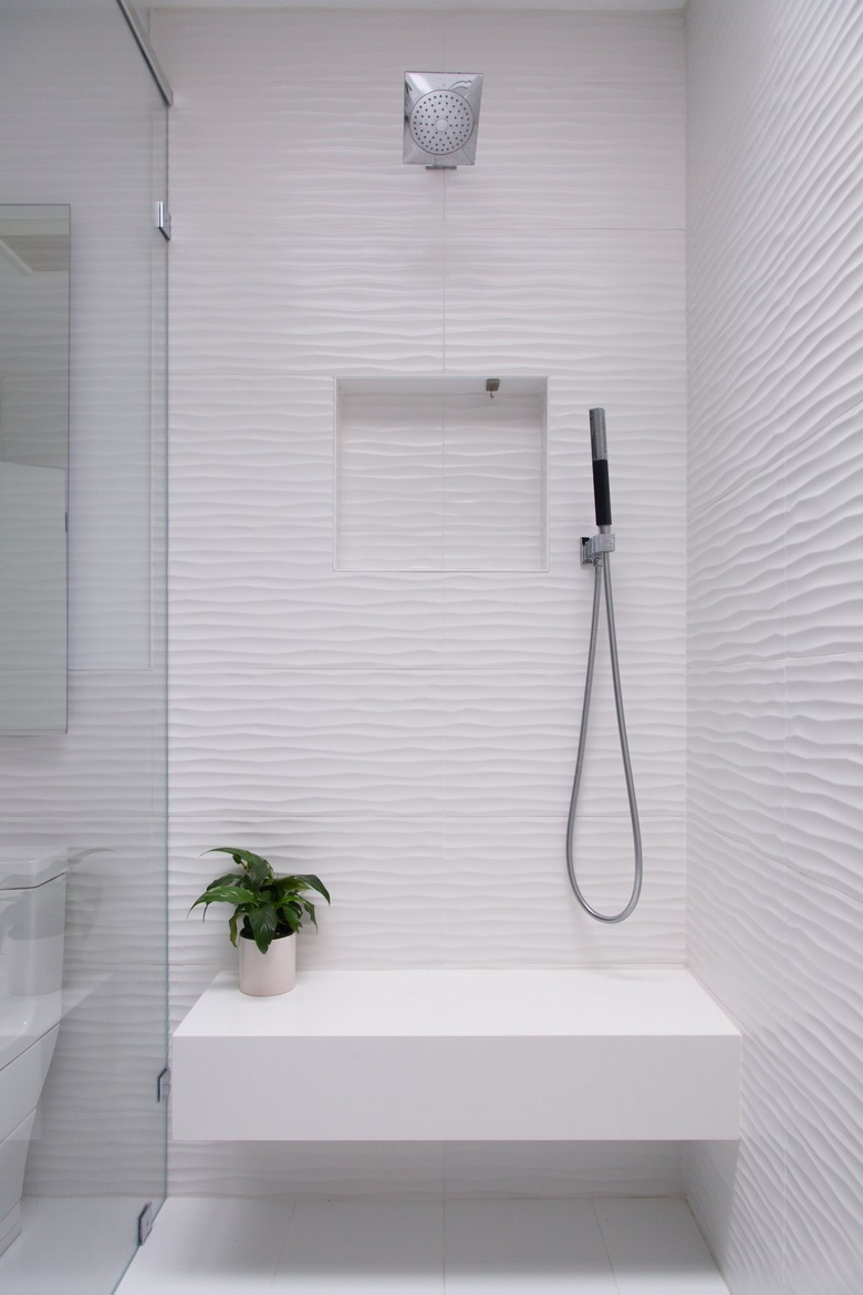 white shower with bench that has a small plant on it