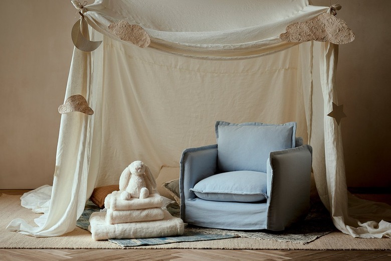 The mini Sixpenny Neva chair in a light blue underneath a fort made from a beige sheet pinned with paper clouds