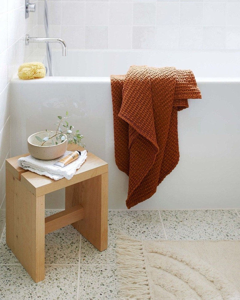 warm neutral boho bathroom with caramel towel thrown over a white bathtub