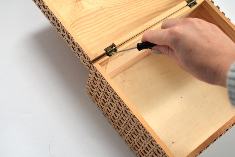 Hand holding screwdriver while screwing lid back onto box.