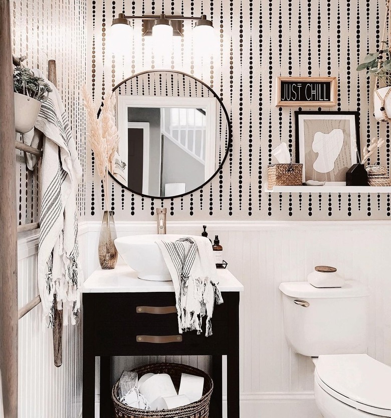 small modern bathroom with black and white wallpaper and round mirror