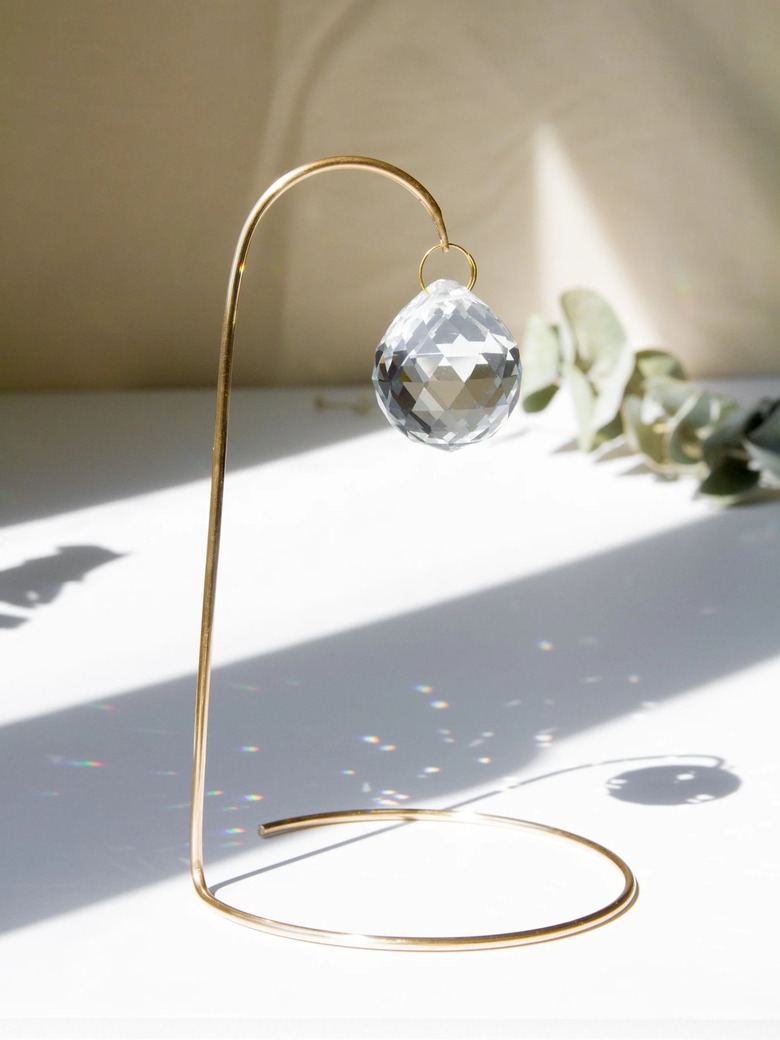 A tabletop wire bent so that it rest on the table and hangs over with a clear crystal that reflects rainbow prisms on the white surface.
