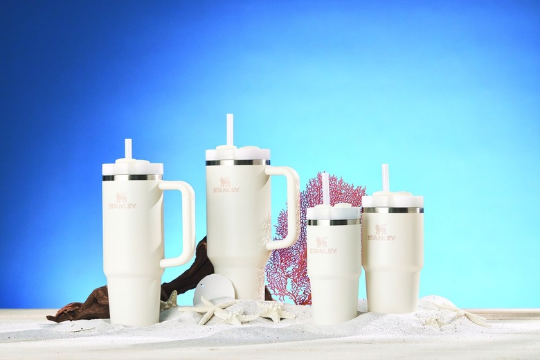 Four cream colored Stanley Quencher Tumblers rest on a small pile of sand amidst starfish