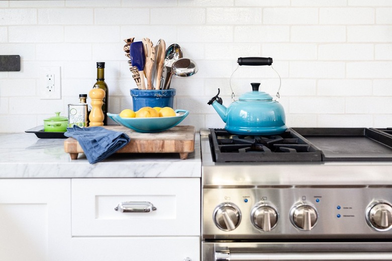 Fireclay white tiles behind stove in kitchen with blue kettle.