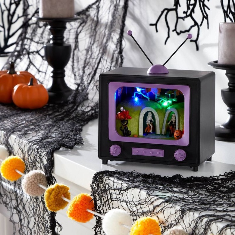 A small prop black and purple TV on a mantel with black spiderwebs