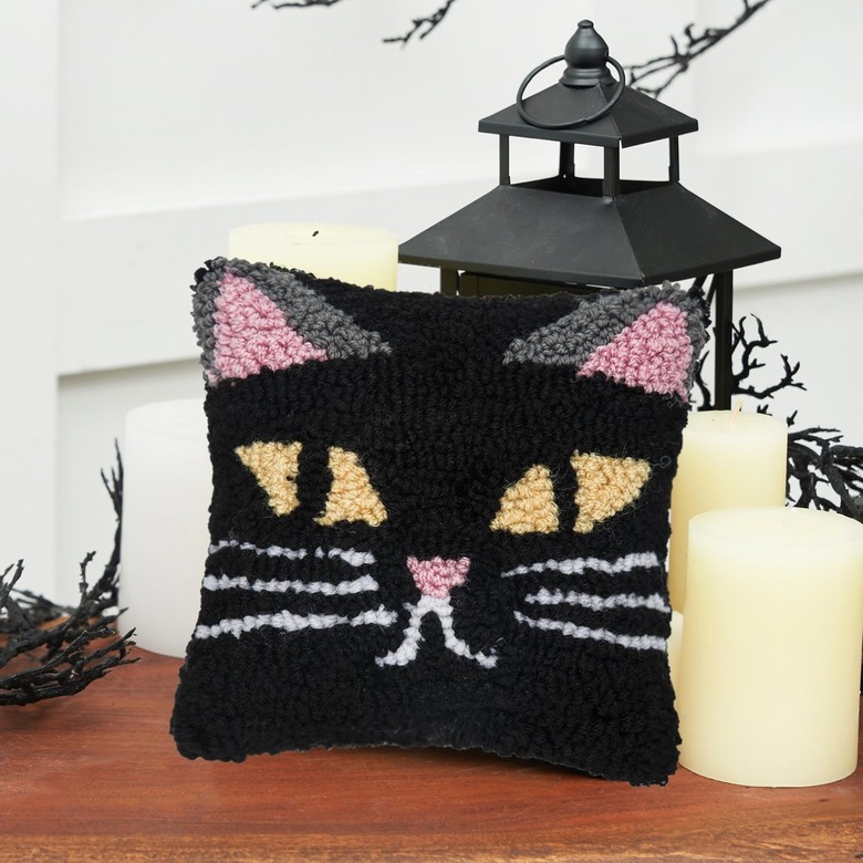 A black tufted square pillow with a cat face on it. The ears are pink and grey