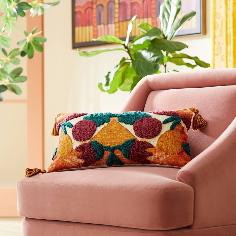 A lumbar throw pillow on a pink fabric armchair. The pillow features abstract green
