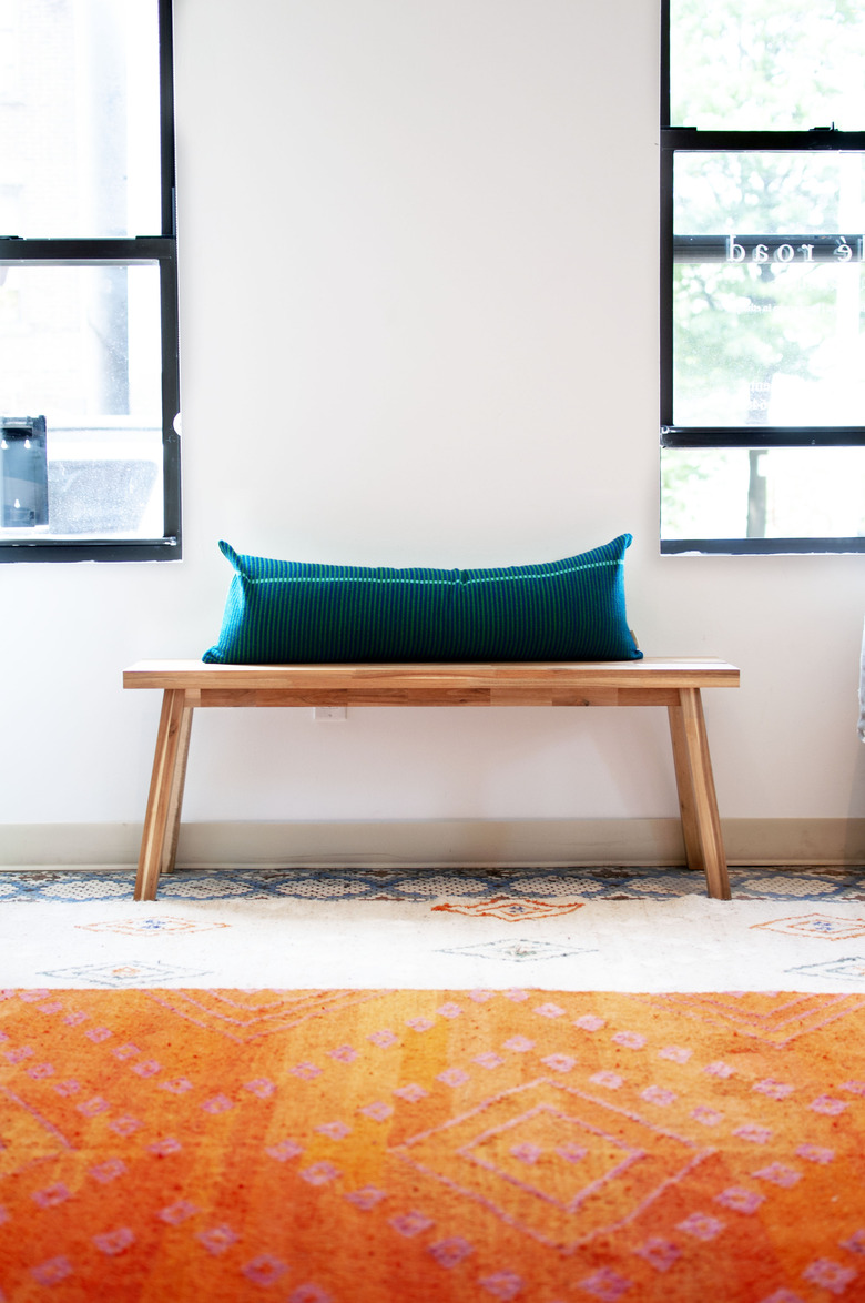 long accent pillow on wooden bench in front of windows