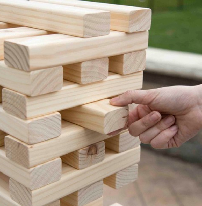 A hand removes a large wooden brick from a stack