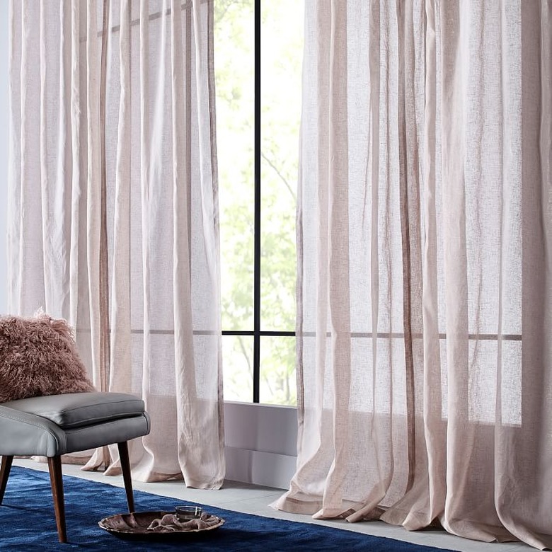 Blush curtains hang next to a gray chair and blue rug.