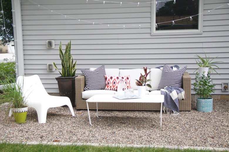 A pea gravel patio with white patio furniture and a multitude of plants