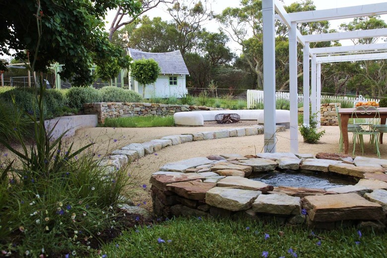 A classic English garden with a pea gravel patio has modern white arbors in it