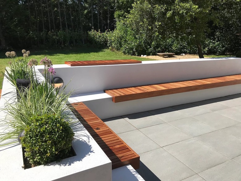 A built-in concrete bench with wood adornment is on top of a concrete patio