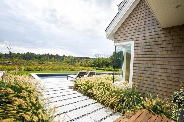 Horizontal concrete pavers lead the way to an in-ground swimming pool near a house with cedar shake siding