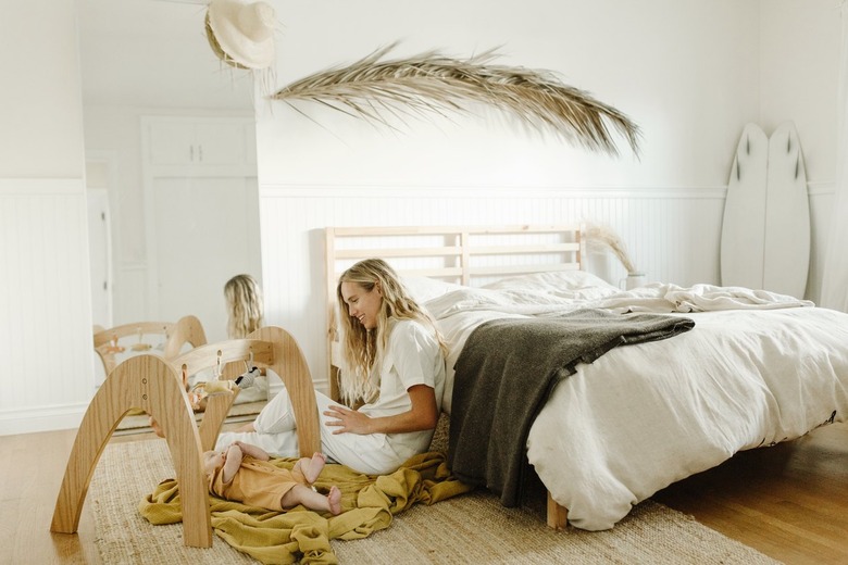 Woman sitting in white boho master bedroom with large wooden children's toys on the floor
