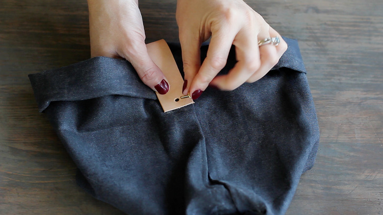 Inserting brass rivet post through hole of leather strip