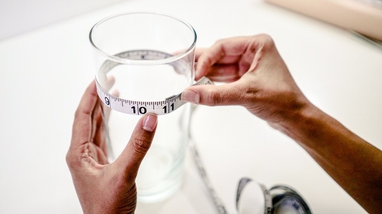 Hands wrapping measuring tape around a clear glass vase