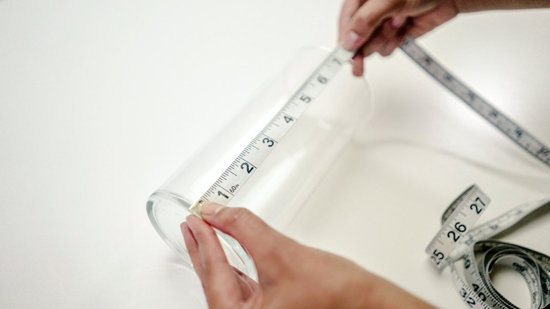 Hands using measuring tape on a clear glass vase