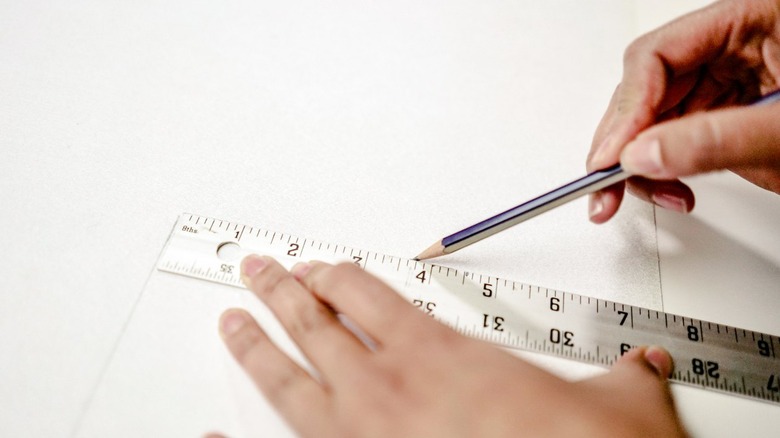 Hands using ruler and pencil on leather