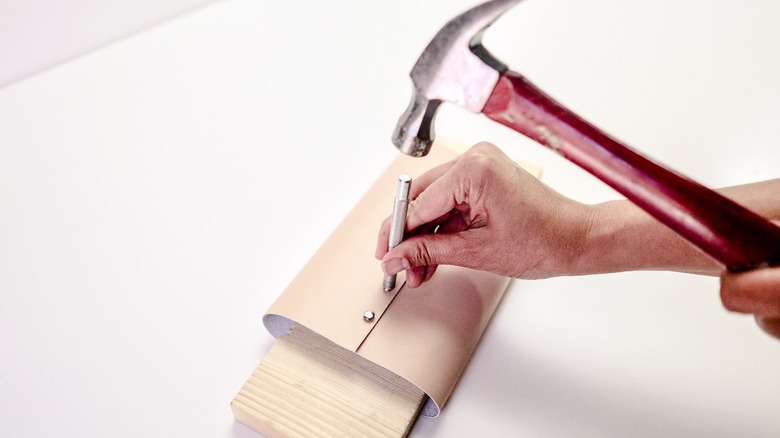 Hand Beige hammering silver rivets in a leather vase with piece of wood